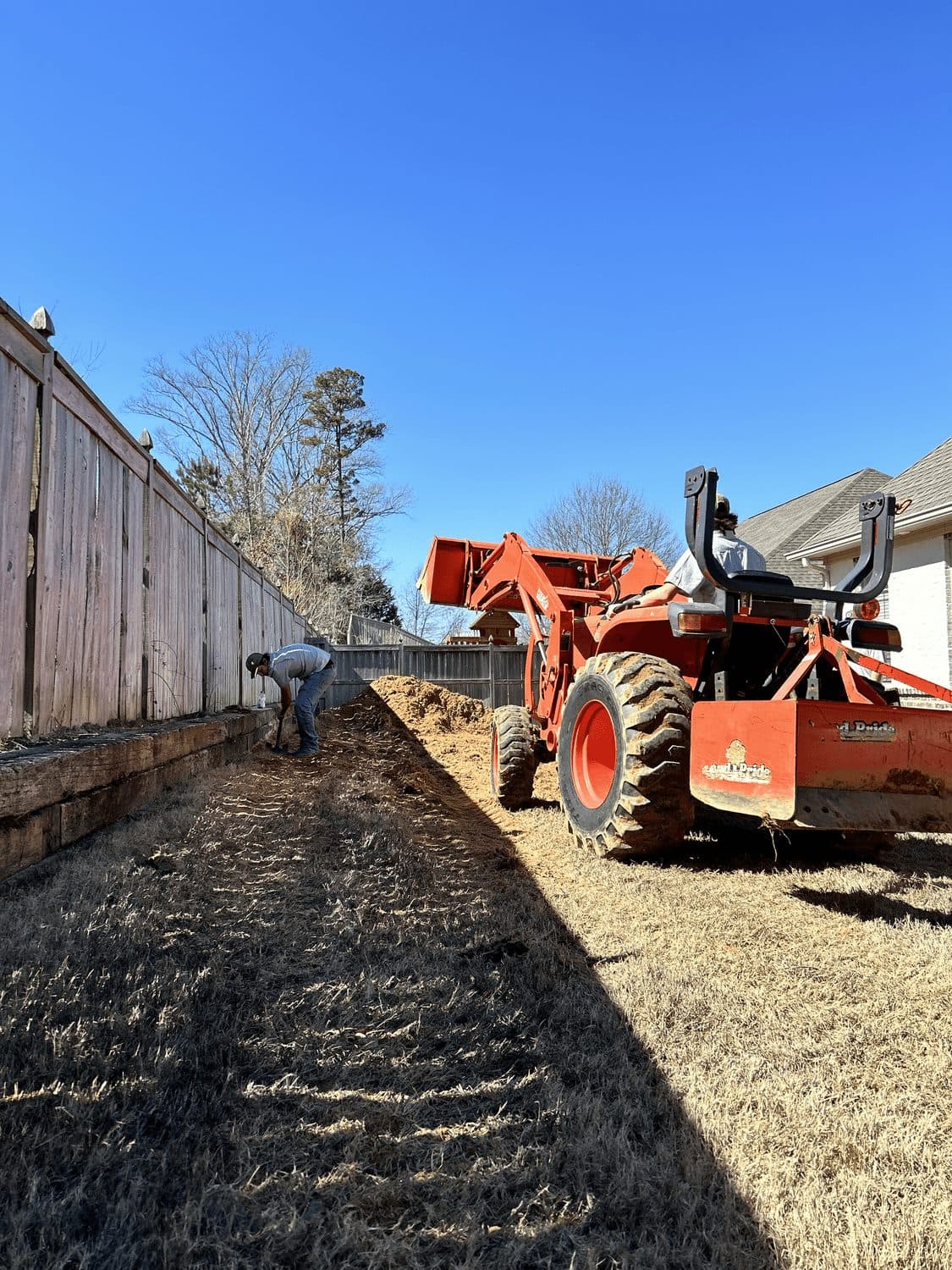 Tractor grading a long strip of yard along a fence