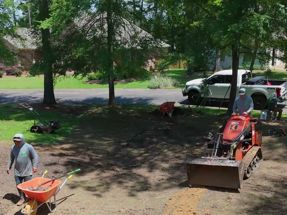 Crew with a wheelbarrow and compact loader doing dirt work on a new yard