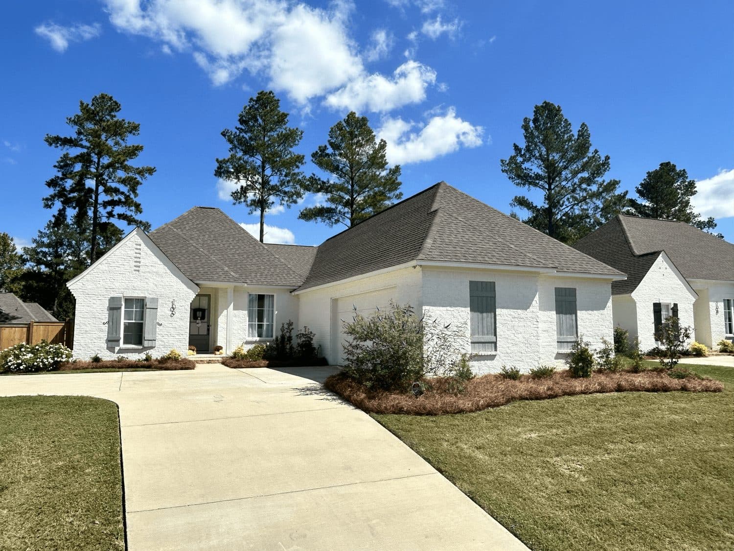 Front lawn and shrub beds at a white brick home under tall pines